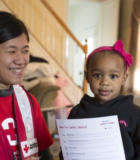 child next to a red cross volunteer holding a safety checklist