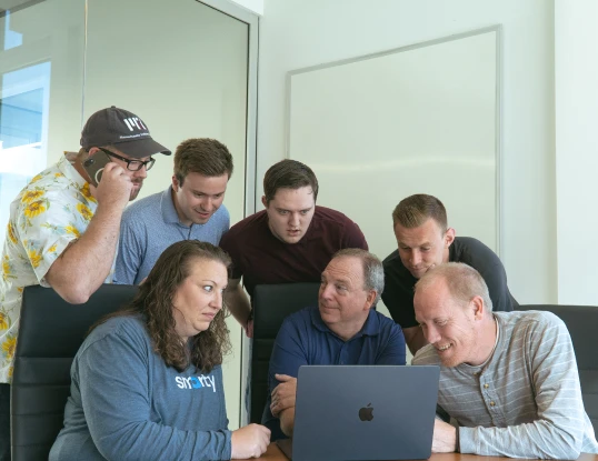 Seven members of the support team gathered around a Macbook, solving problems.
